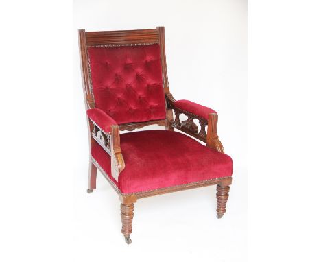 A late Victorian caved walnut gentleman's library chair, with button back claret coloured draylon upholstery, on turned legs,