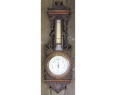 A Victorian carved oak aneroid barometer, with silvered dial signed by the retailer Charles W Coe, and thermometer with brass