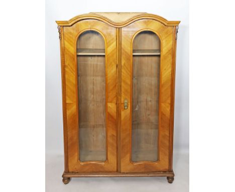 Vitrine. Nussbaumfurnier. 2-türig verglaster Korpus. Geschnitzter Aufsatz (erg.). Schloss mit Schlüssel vorhanden. Alters- un