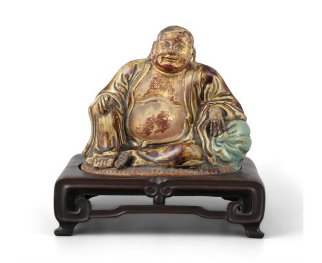 AN ENAMELLED MOULDED CERAMIC SCULPTURE OF A SEATED BUDAIChinaBudai is depicted seated in rajalalisana, his left hand on a pou