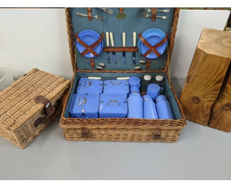 A Coracle picnic hamper with various containers, plates, cups, flask, knives and forks, a wicker basket and a wooden blockLoc