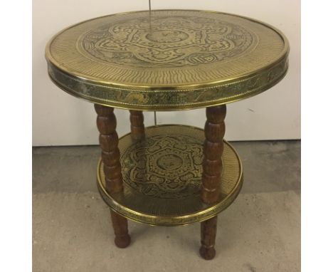 An oriental brass and wood circular table. Brass top and lower shelf with oak legs. 60cm diameter.