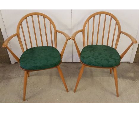 A pair of Ercol blonde stick back armchairs. With green padded seats. 