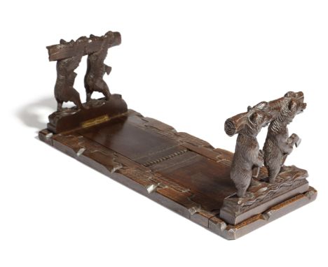 A Black Forest carved wood bookslide, the hinged folding ends each carved with a pair of lumberjack bears, one holding an axe