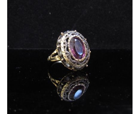 A gold ring centrally set with pink stone in ornate pierced and swag frame with old cut diamonds to outer. Size H, 6.3g