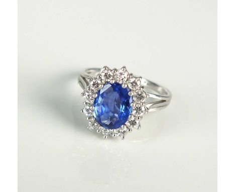 An oval sapphire and diamond cluster ring, designed as a central oval mixed cut sapphire claw set within a border of twelve b