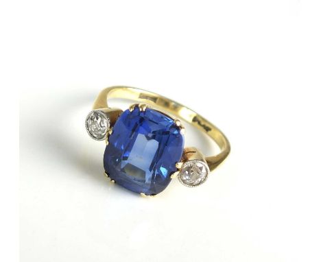 A three stone synthetic sapphire and diamond ring, designed as a central cushion cut synthetic sapphire claw set in yellow me