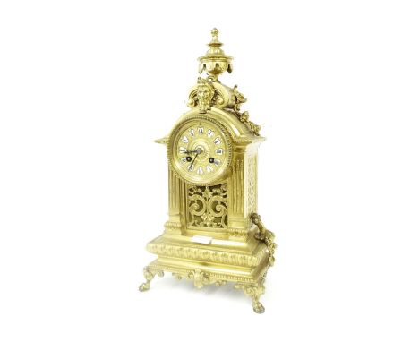 Brass two train mantel clock striking on a bell, the 3" repousse dial with cartouche Roman enamel numerals, within a rounded 