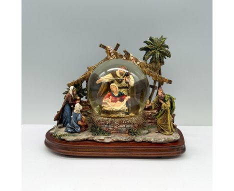 On a wooden base, a matte figurine featuring Jesus, Mary, and Joseph inside a snow globe, with the three wise men beside them