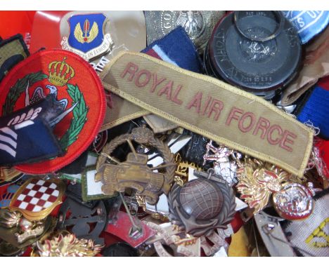 An assortment of military cap badges and insignias, cloth and metal- with some reproductions, together with a compass belt bu