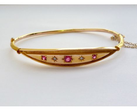 An Edwardian 9ct gold, ruby and diamond hinged-bangle, having a lenticular shaped face with an incised border of engine-turne
