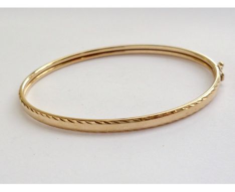 A slender 9ct gold hinged bangle, having bright-cut feather edging, 4.4g total
