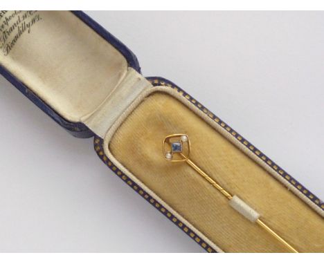 An Edwardian sapphire and pearl stick pin, the openwork terminal of rounded rectangular form centrally set with a princess-cu