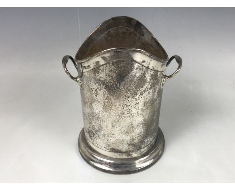 An Edwardian silver Arts and Crafts syphon / bottle stand, having planished decoration and an incised whiplash border termina