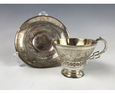 A late 19th Century Russian parcel-gilt white-metal tea cup and saucer, having a reticulated bracket handle, decorated with e