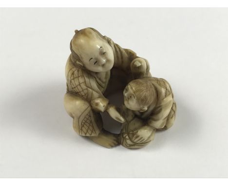 A Meiji Japanese carved ivory netsuke modelled as a crouching man giving assistance to a weary traveller, character marks to 