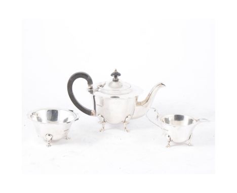 A George V silver three piece bachelor teaset, plain polished cut edge design on three or four pad feet, ebony handle and fin