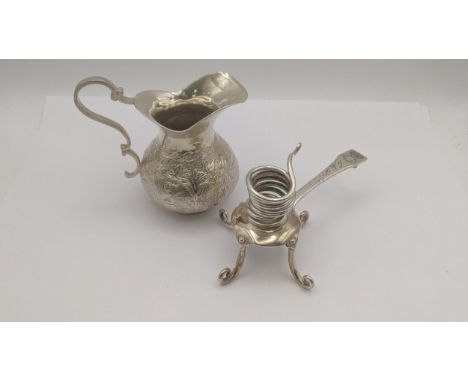 A white metal cream jug decorated with floral and figural decoration, along with a white metal usual chamber stick  engraved 