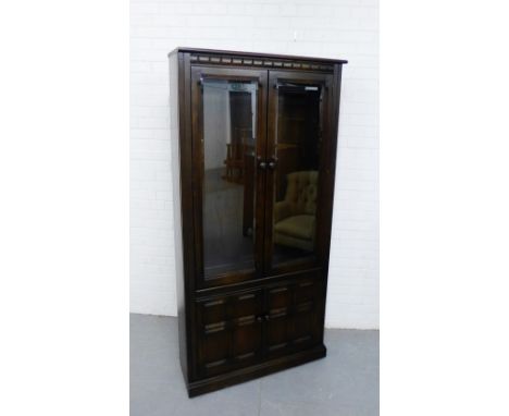 A dark elm Ercol bookcase cabinet, the carved cornice over a pair of glazed doors and two panelled cupboard doors to the base