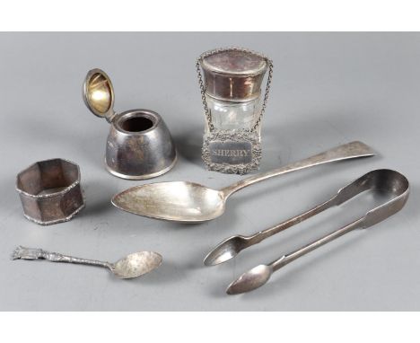 A pair of silver sugar tongs, a silver tablespoon, a silver napkin ring, a silver inkwell, a silver bottle ticket and a cut g