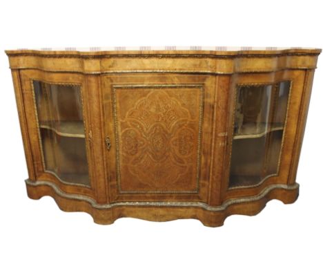 A Victorian walnut serpentine shaped credenza the central foliate inlaid door enclosing baise shelf interior flanked by a pai