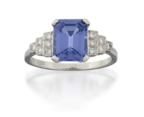 the emerald-cut tanzanite in a white four claw setting, to stepped round brilliant cut diamond set shoulders, on a plain poli