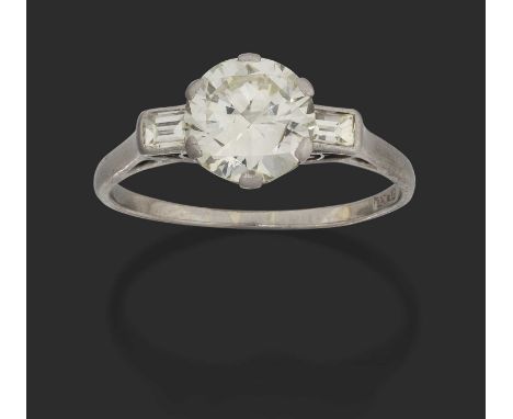 the round brilliant cut diamond in a white claw setting, flanked by baguette cut diamonds in rubbed over settings, to a taper