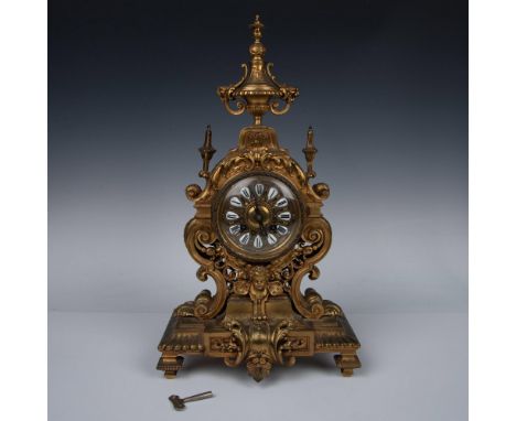 This antique mantle clock, meticulously crafted from brass, boasts a square base topped with an hourglass silhouette. Adorned