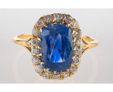 A sapphire and diamond cluster ring, claw set to the centre with an oval cushion-cut sapphire with blue to violet hues, (poss
