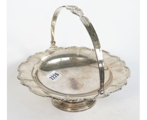 A silver cake or fruit basket, of shaped circular form, having a decorated rim, with a swingover handle, raised on a circular