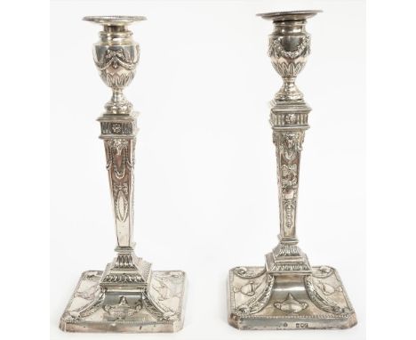 Two similar silver table candlesticks, each with a tapered square section stem, raised on a cut cornered square base, decorat