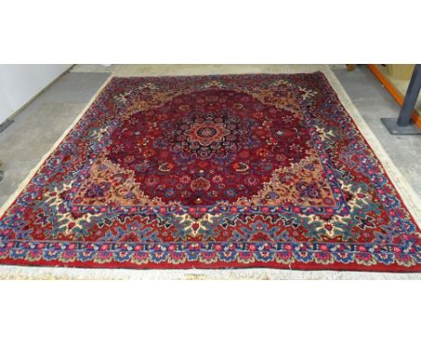 A Mashad carpet, Persian, the dark madder field with a black and madder rosette medallion, fawn spandrels, all with trailing 