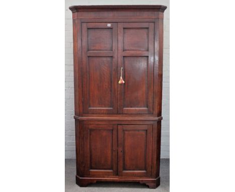 A mid-18th century oak double height floor standing corner cupboard with two pairs of panel doors on bracket feet, 105cm wide