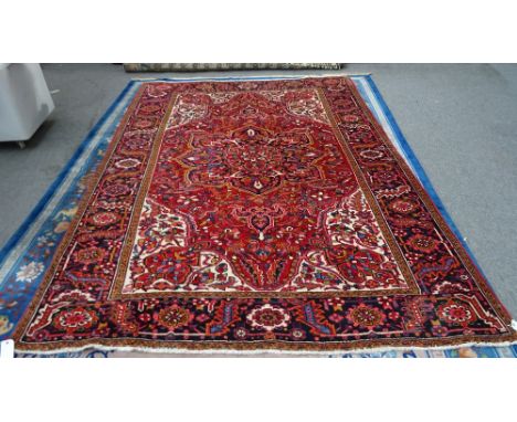 A Heriz carpet, Persian, the madder field with a bold dark indigo medallion, ivory spandrels, all with angular leaves, vines 