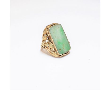 A gold and jade ring, the rectangular jade panel with carved and pierced decoration, the shoulders pierced with floral, folia