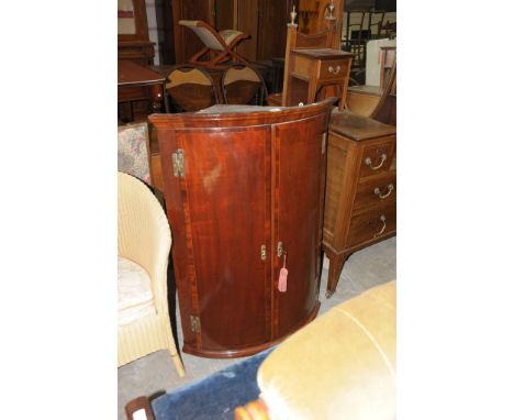 A George III mahogany and cross banded bow front hanging two door corner cupboard with H brass hinges.