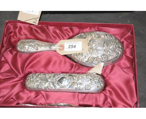 A silver plated cased vanity set Embossed with foliate decoration, comprising; comb, hair brush and clothes brush, together w