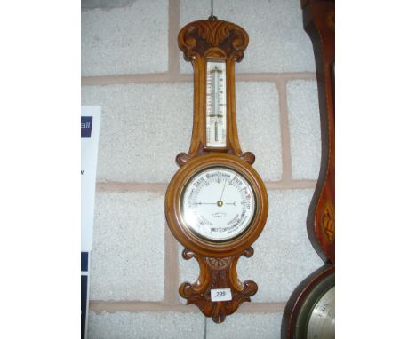 A Late Victorian carved oak wall barometer with a fitted thermometer and a white enamelled dial signed " T Woolley , Chester 
