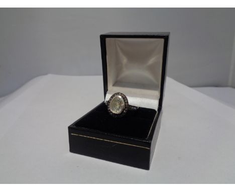 A CONTINENTAL WHITE AND YELLOW METAL RING WITH CENTRE DIAMOND AND SMALLER SURROUNDING DIAMONDS WHICH CONTINUE ON THE SHOULDER
