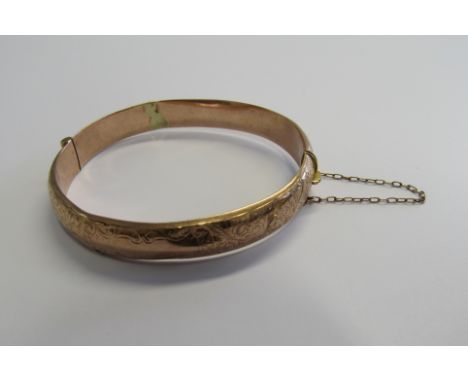 An Edwardian rose gold bangle with half patterned foliate scroll and blank cartouche. Hallmarked 9ct, Birmingham 1910. Bangle