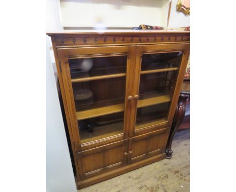 A modern Ercol medium elm bookcase cabinet with glazed top doors and cupboard base 