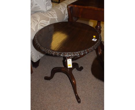 A reproduction mahogany circular occasional table with carved decoration, raised on tripod feet.