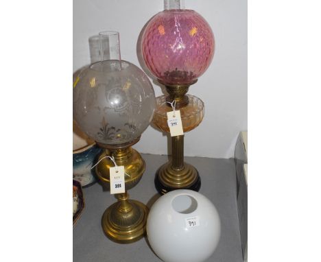 An oil lamp with acid etched shade and brass stand; and another oil lamp with pink glass shade and clear glass reservoir, on 