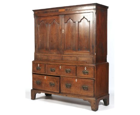 A Georgian oak cupboard on chest. With shaped cornice above two twin arched panelled doors enclosing a re-fitted internal she