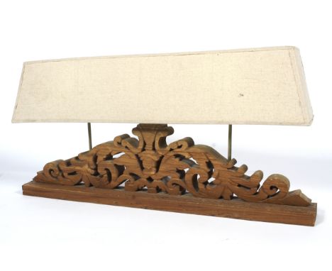 A large carved wooden table lamp. With pierced scrolled wooden base issuing three lights, with long elongated buff linen cove