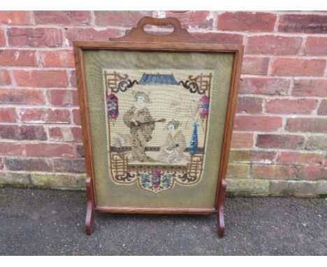 AN OAK FRAMED ORIENTAL THEMED TAPESTRY FIRESCREEN, the decorative glazed tapestry depicting two Geisha in typical costume, ov