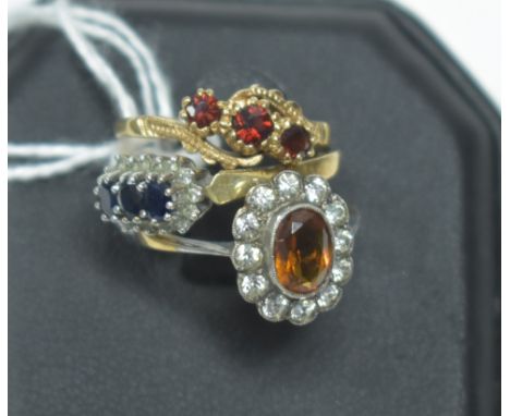 Three rings: a three-stone garnet ring; a sapphire and white stone cluster ring, both on 9ct gold shanks; and an orange and w