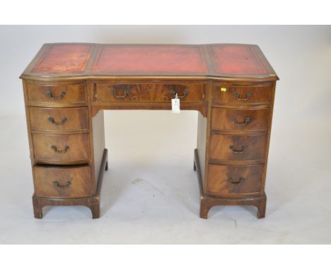 A 20th Century mahogany inverted breakfront desk, with inset red leather writing surface above a central frieze drawer flanke