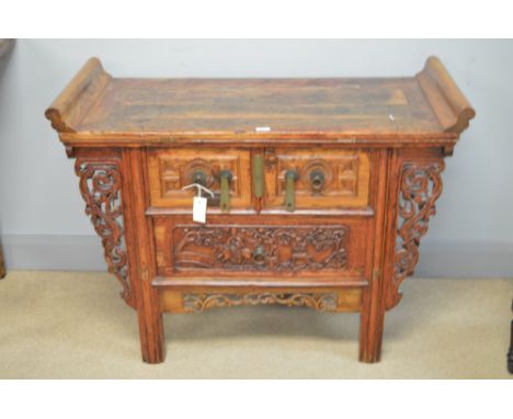 A late 19th/early 20th Century Chinese hardwood altar table, the scroll-over top above a pair of cupboard doors and single dr