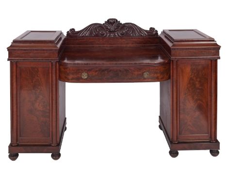 A Regency mahogany pedestal sideboard, early 19th century; with scrolling foliate carved back above the bowfront top, a drawe